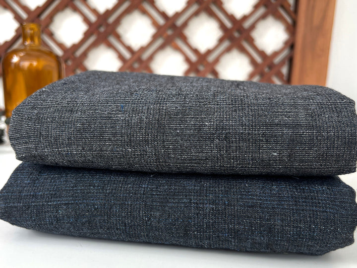 Two folded dark gray fabrics stacked on a white surface with a wooden lattice background.

